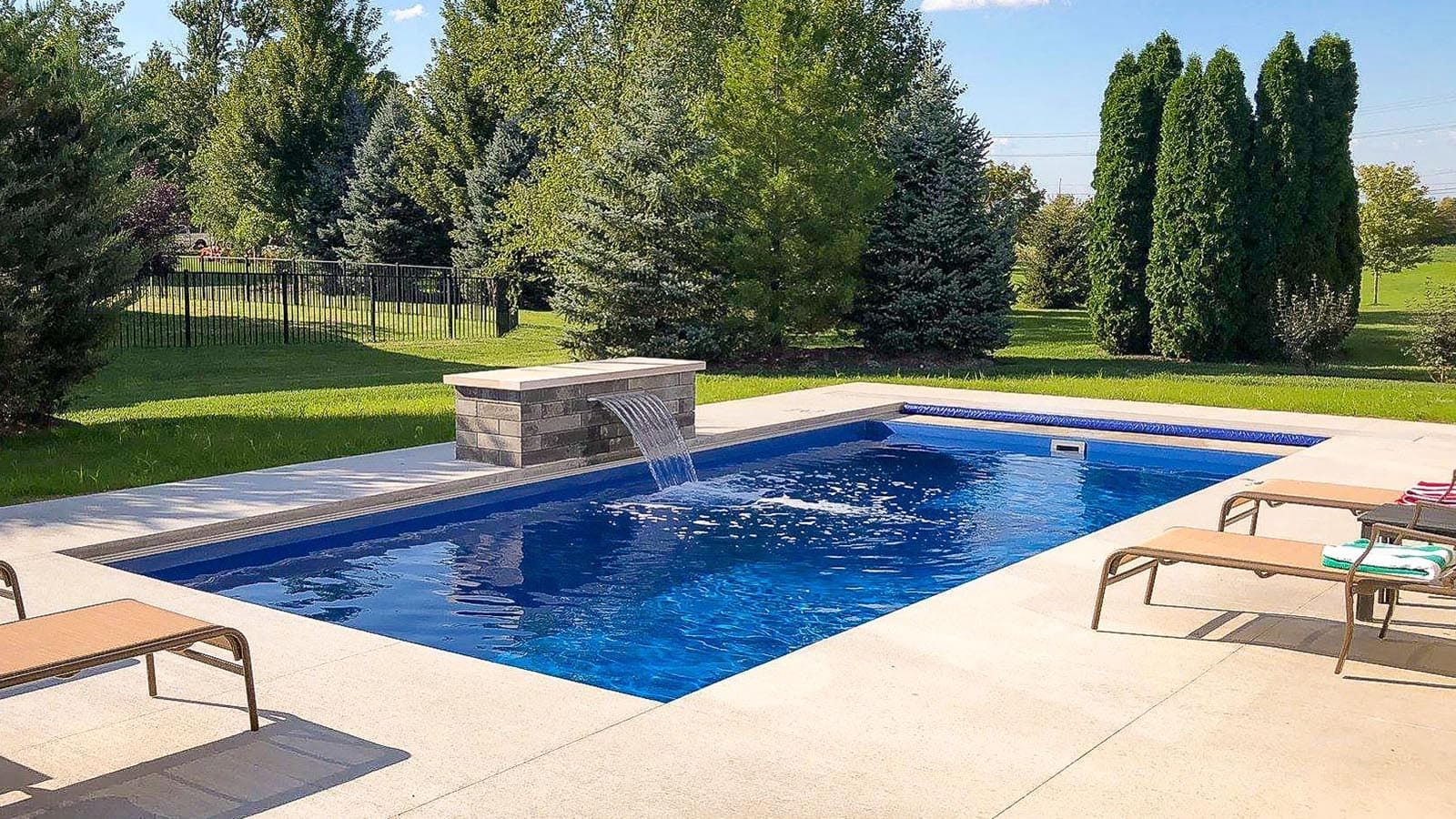 Backyard swimming pool with blue water, stone feature, lounge chairs, and trees in the background