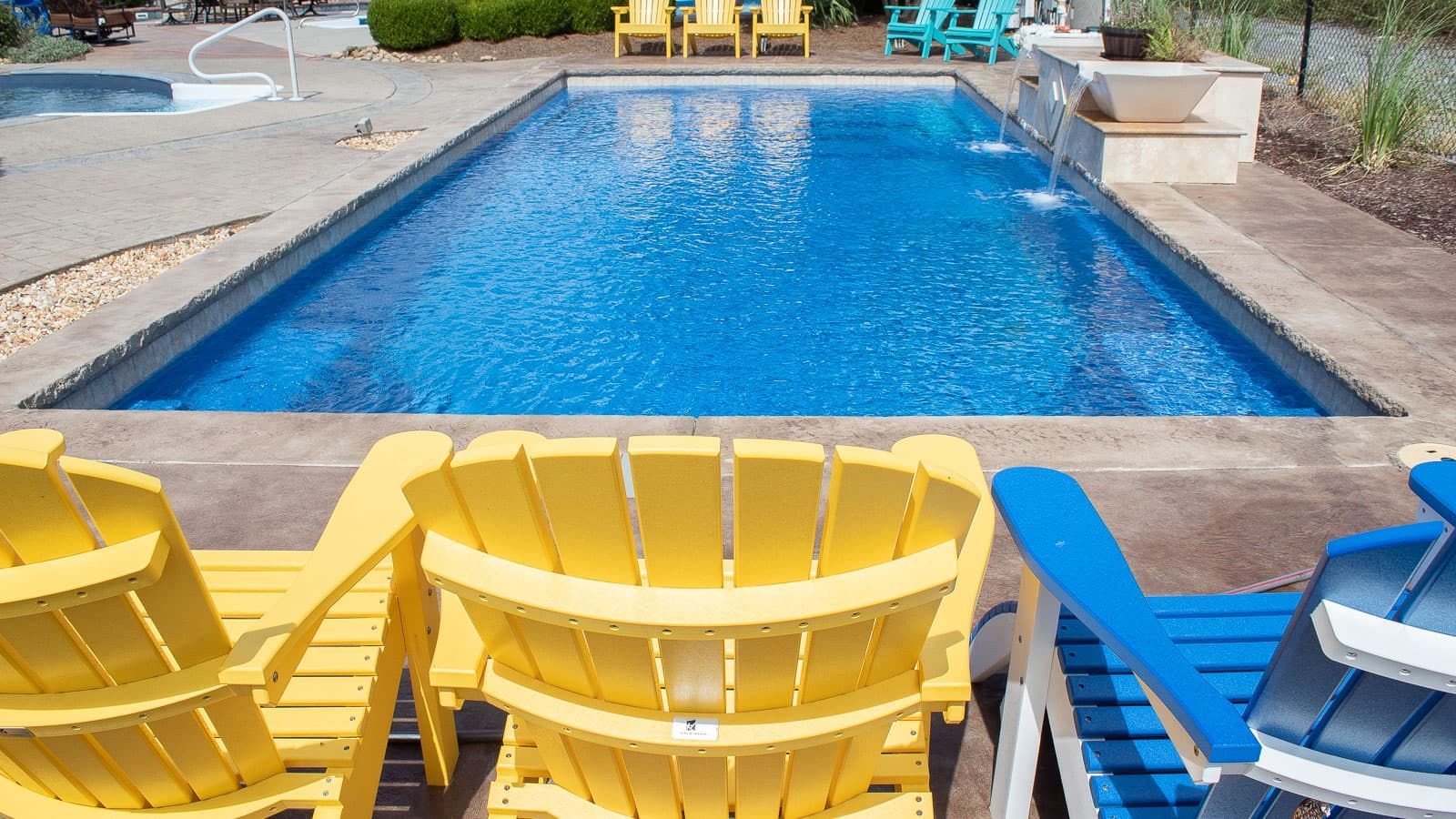 Bright blue swimming pool with yellow and blue lounge chairs on a patio around it