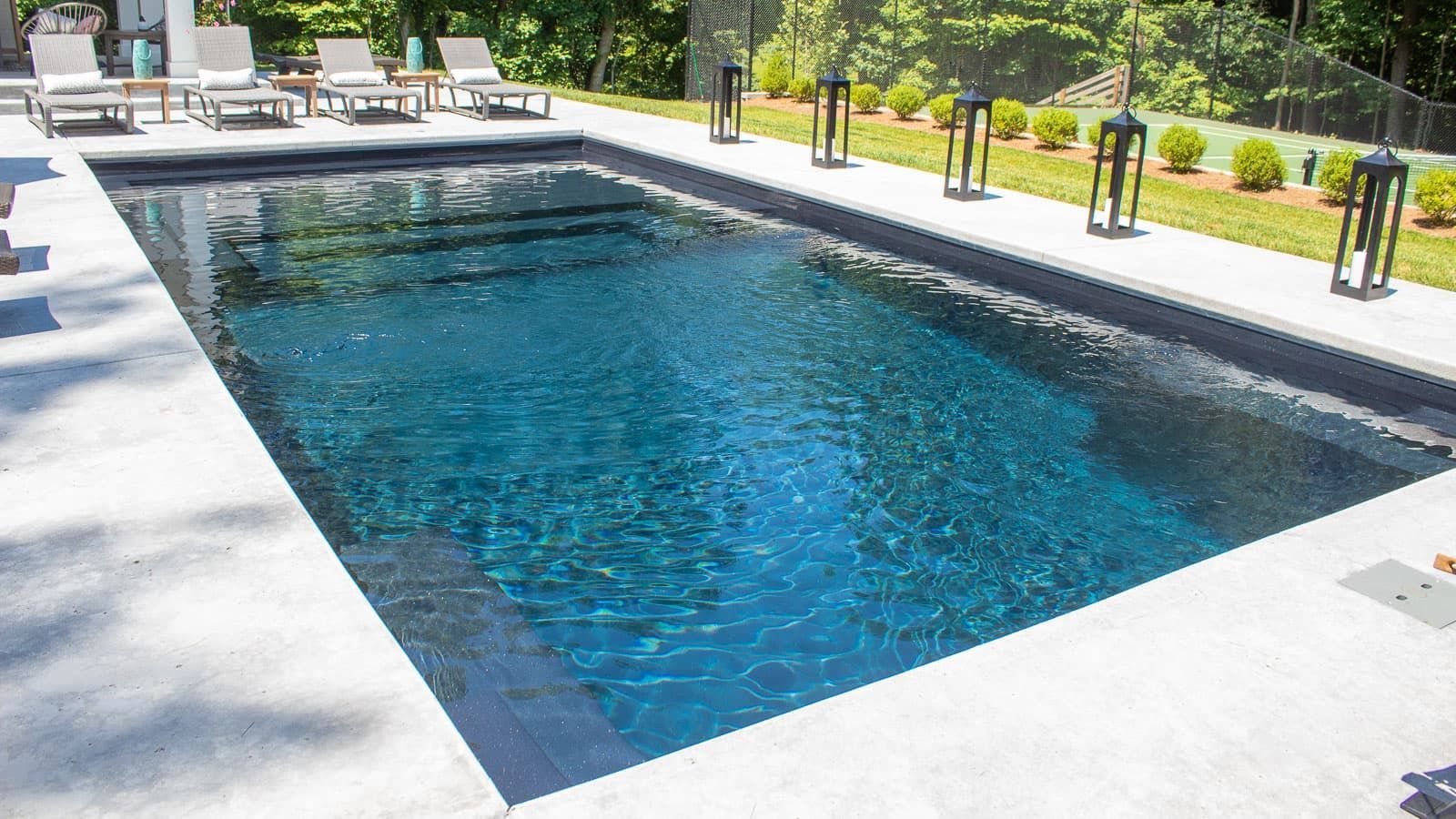 Rectangular outdoor swimming pool with blue water, surrounded by lounge chairs and greenery.