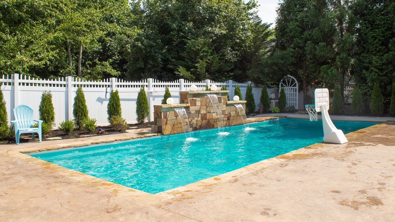 Backyard swimming pool with blue water, stone waterfall, white fence, and lounge chairs
