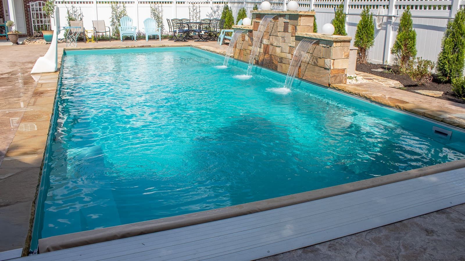 Rectangular backyard pool with turquoise water, stone deck, and lounge chairs in bright sunlight