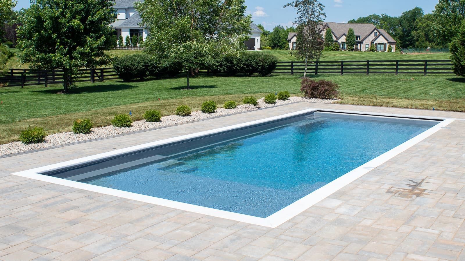 Rectangular backyard swimming pool with blue water beside a stone patio and green lawn