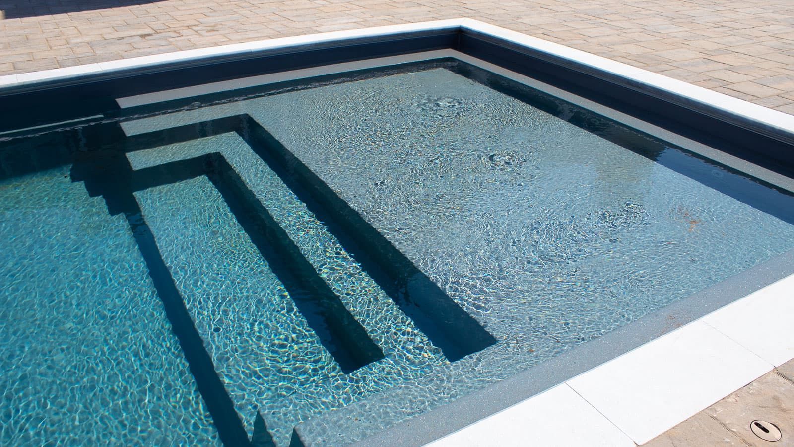 Small rectangular backyard pool with blue water, white tile edge, and dark built-in steps at one end