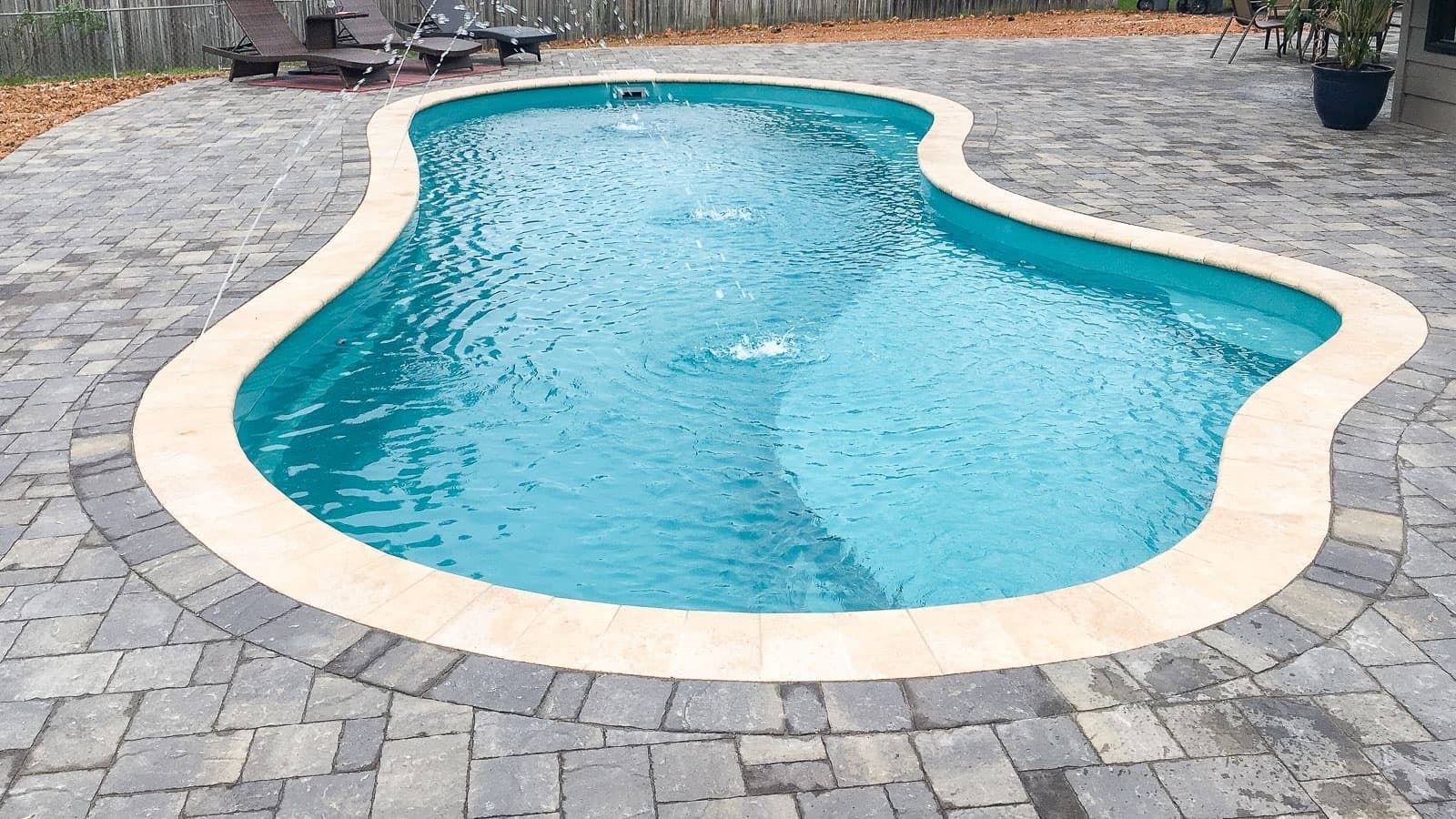 Curved backyard swimming pool with turquoise water and a stone paver deck