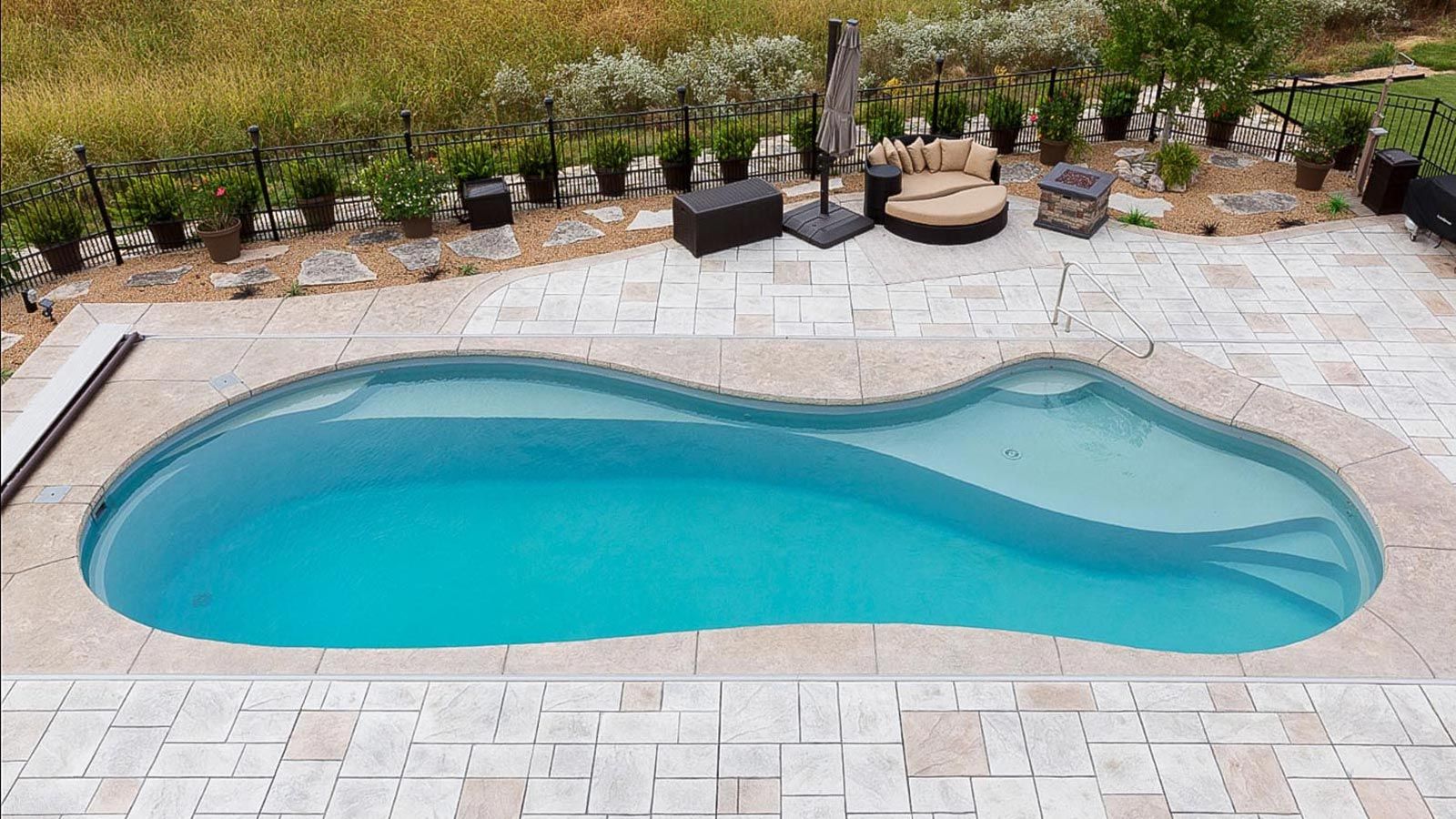 Backyard swimming pool with light blue water, bordered by stone pavers and plants along the edge