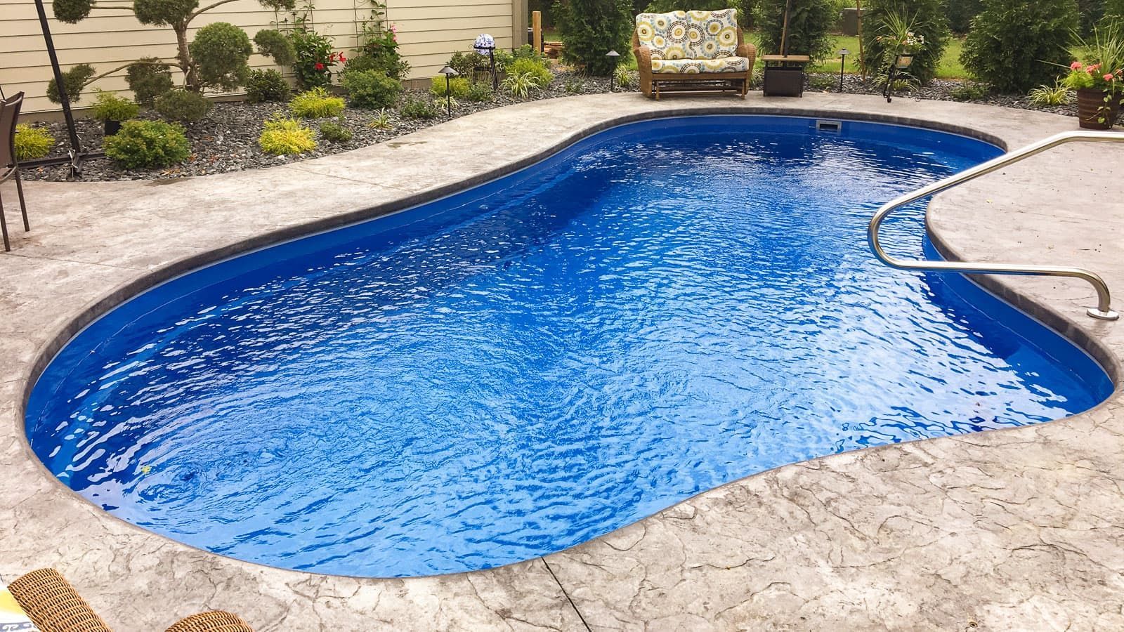 Blue backyard swimming pool with stone patio and landscaped garden around it