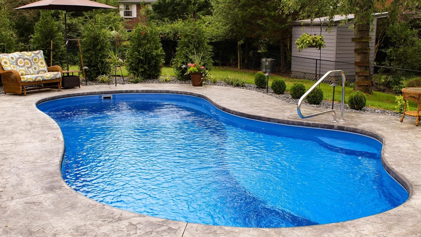 Backyard swimming pool with blue water, stone deck, lounge chairs, and greenery around it