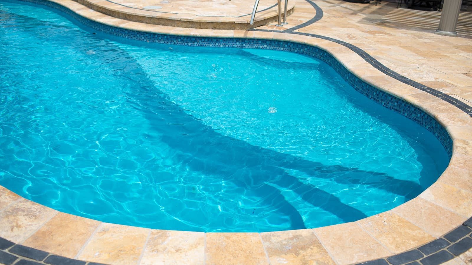 Curved blue swimming pool with beige stone decking and shimmering water