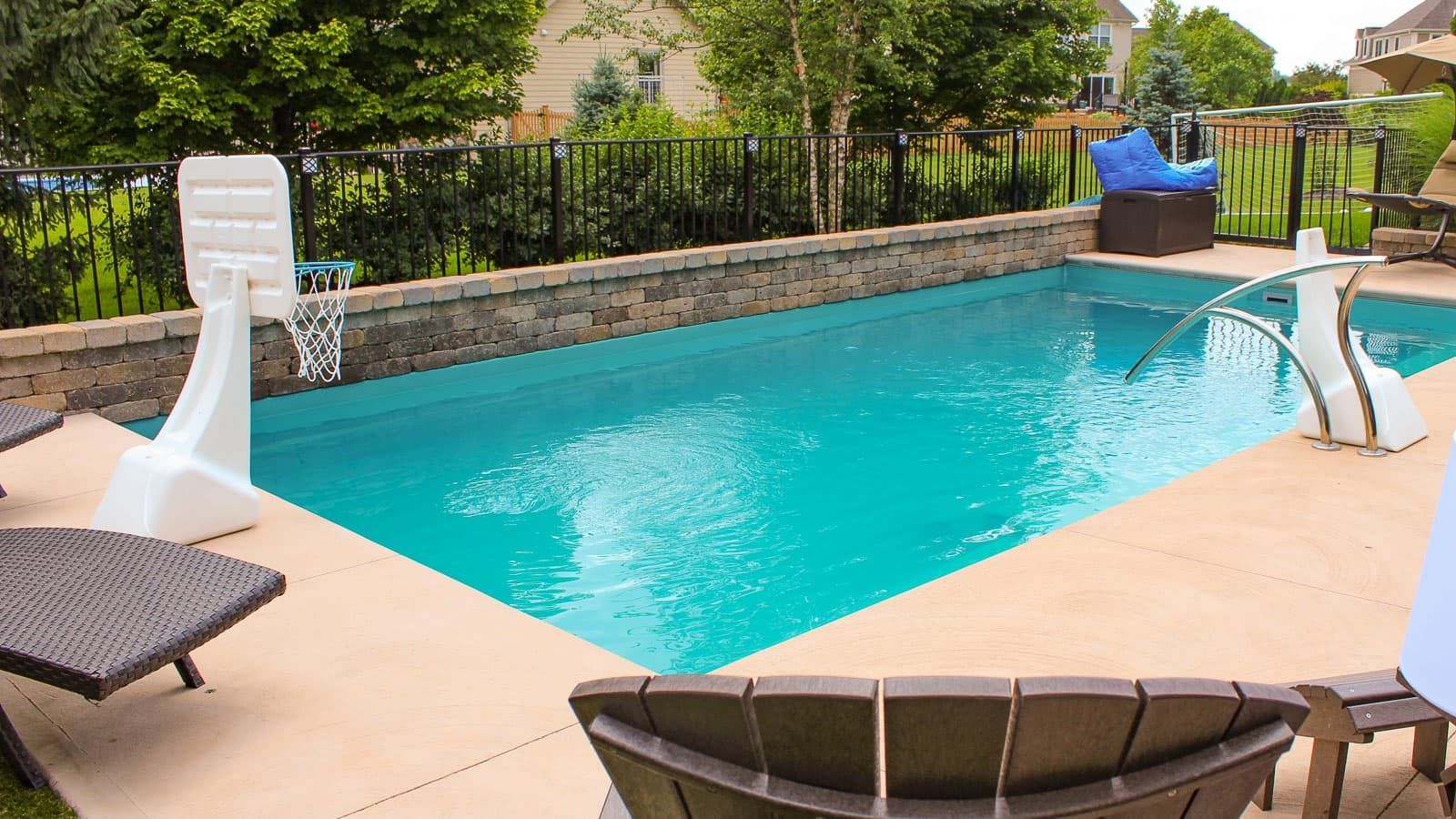 Backyard swimming pool with turquoise water, tan deck, lounge chairs, and garden greenery