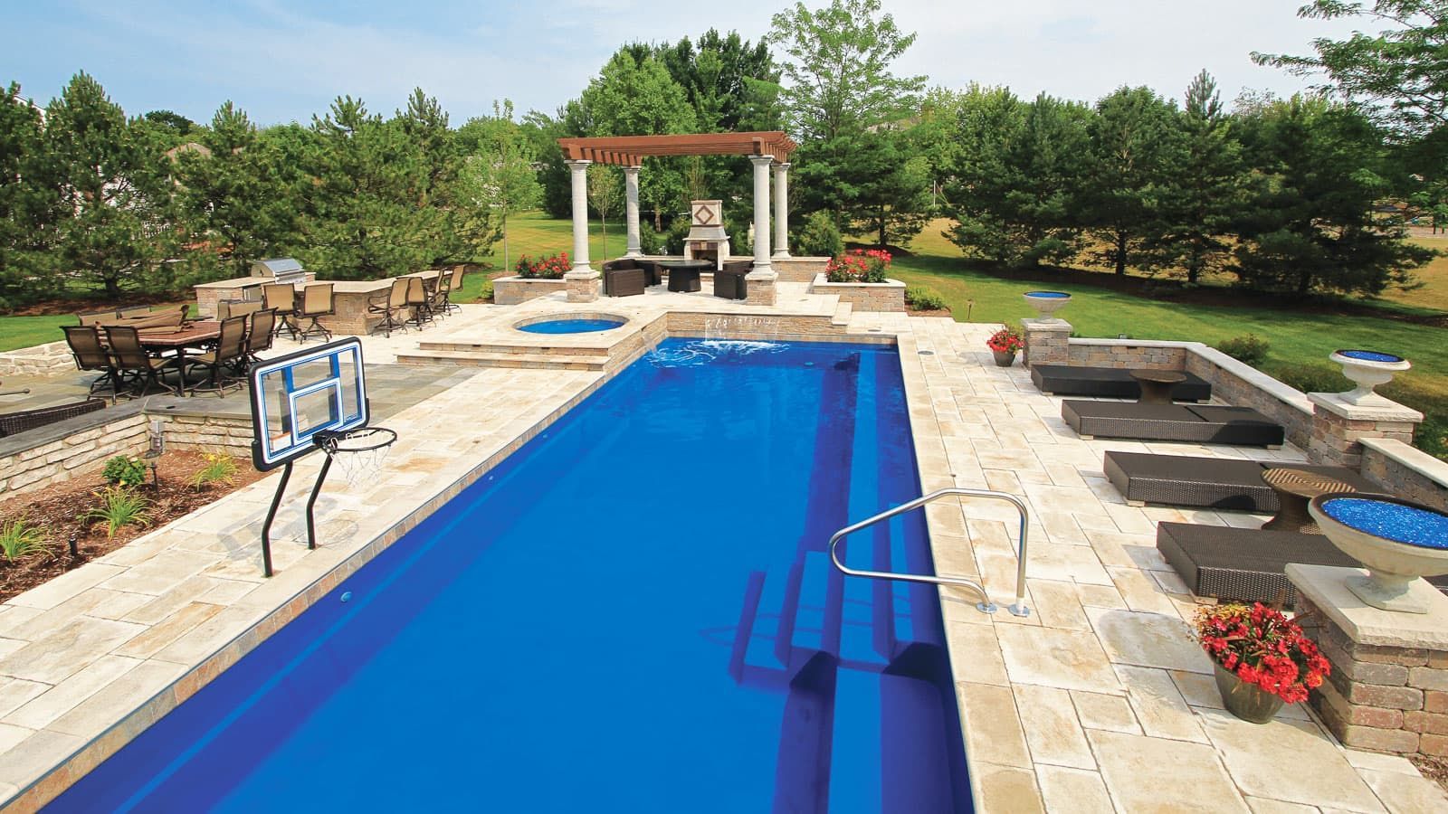 Backyard swimming pool with stone patio, lounge chairs, and a pergola in a landscaped yard