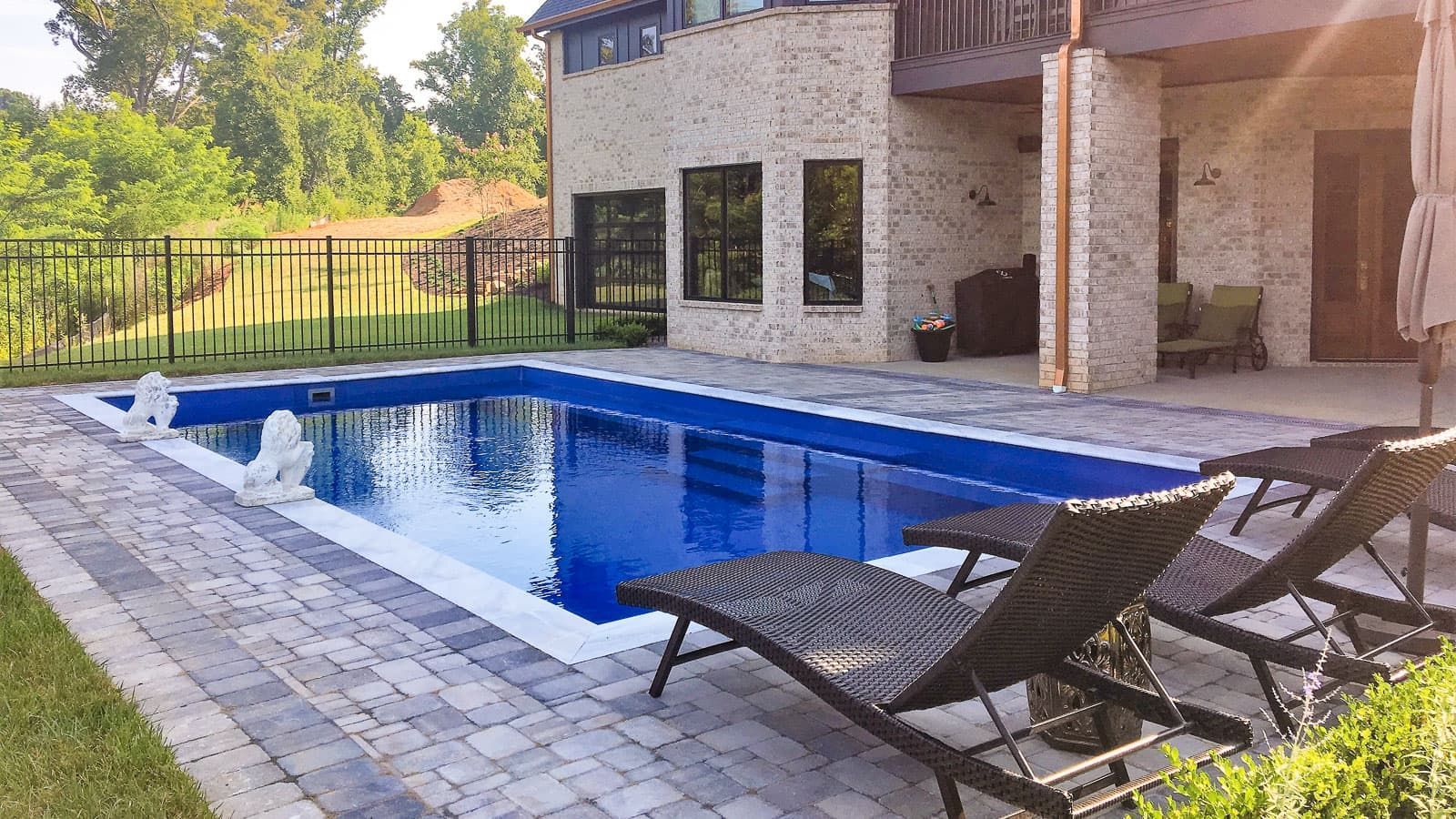 Backyard pool beside a stone house, with lounge chairs on a sunny patio