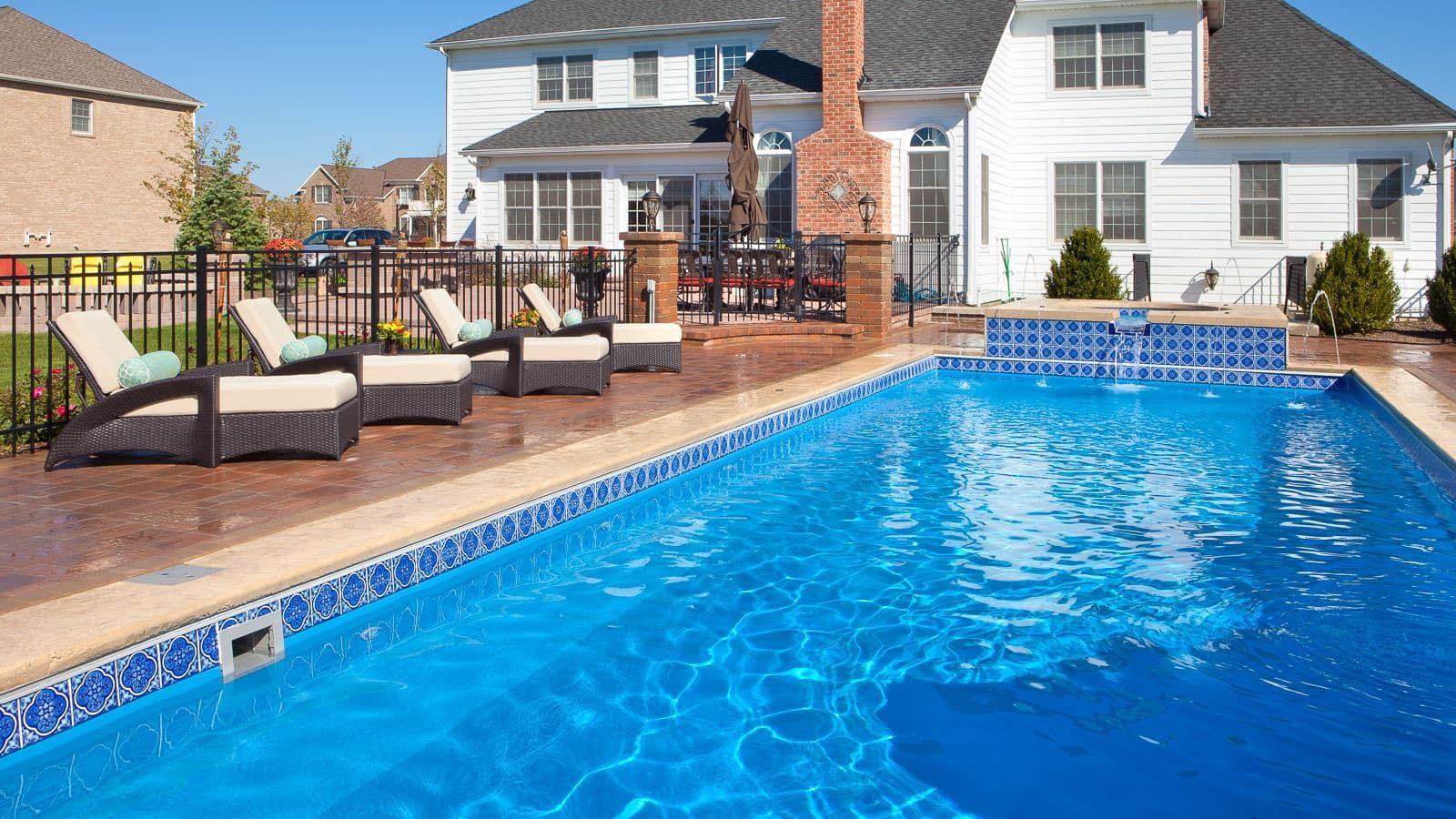 Backyard pool with blue water, patio seating, and a white two-story house in the background