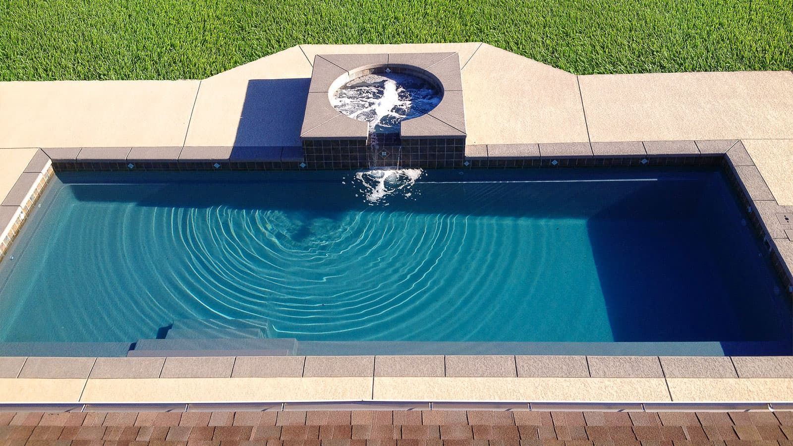 Small rectangular backyard pool with blue water and a stone waterfall feature at one end