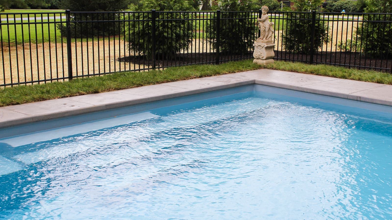Outdoor swimming pool with clear blue water beside a fenced grassy yard