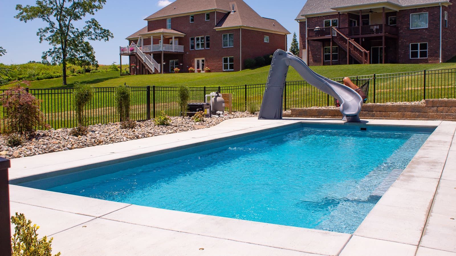 Backyard swimming pool with a slide, patio, and large houses in the background