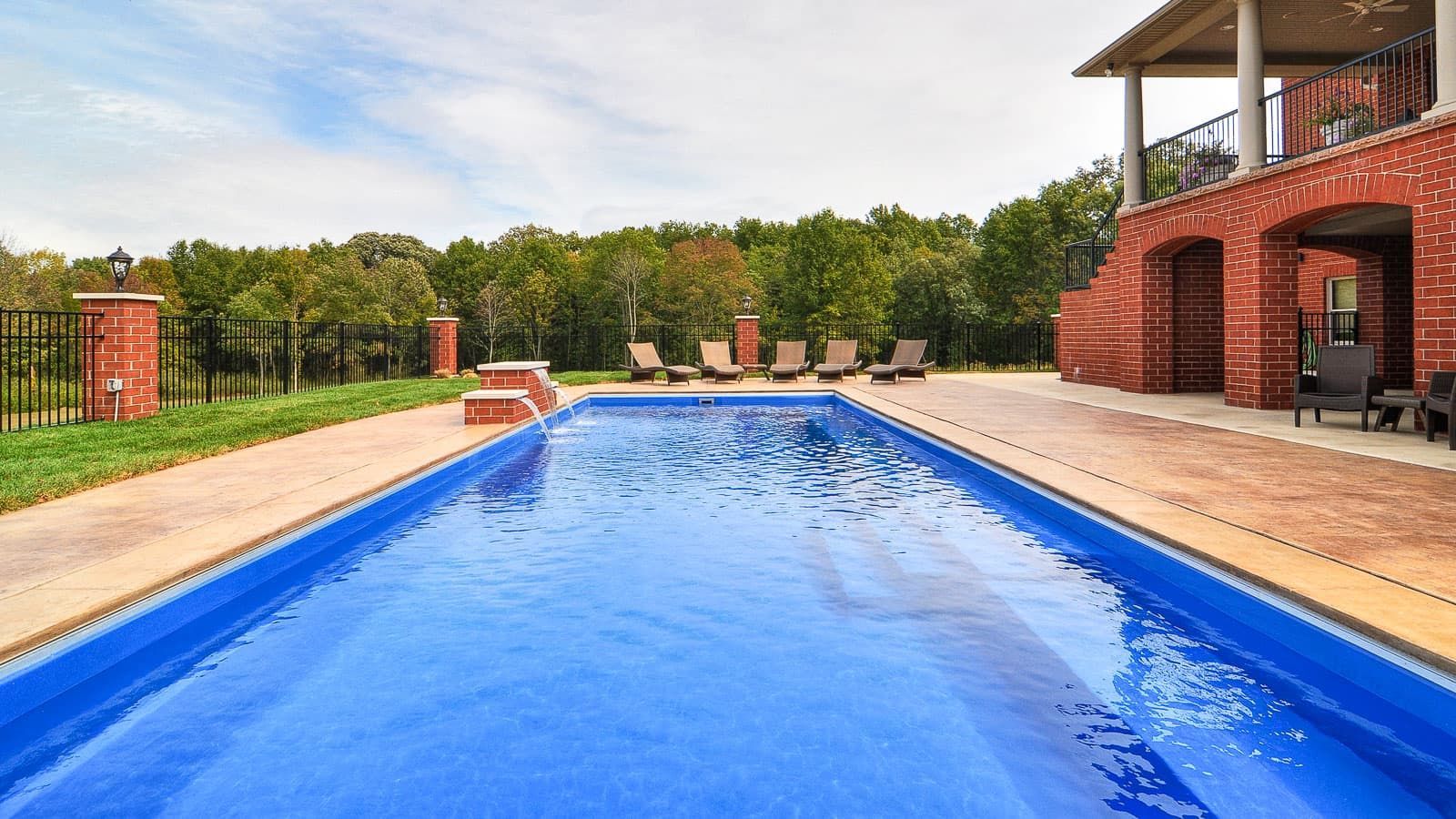 Long backyard pool with bright blue water beside a red brick patio and house
