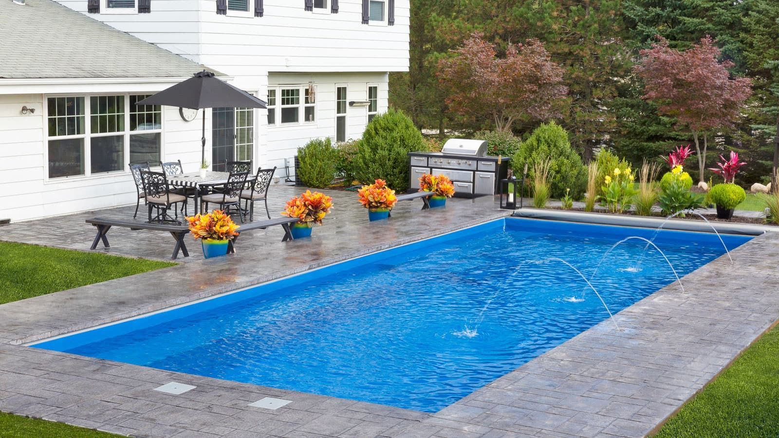 Backyard with a rectangular in-ground pool, patio chairs, and a white house surrounded by landscaping