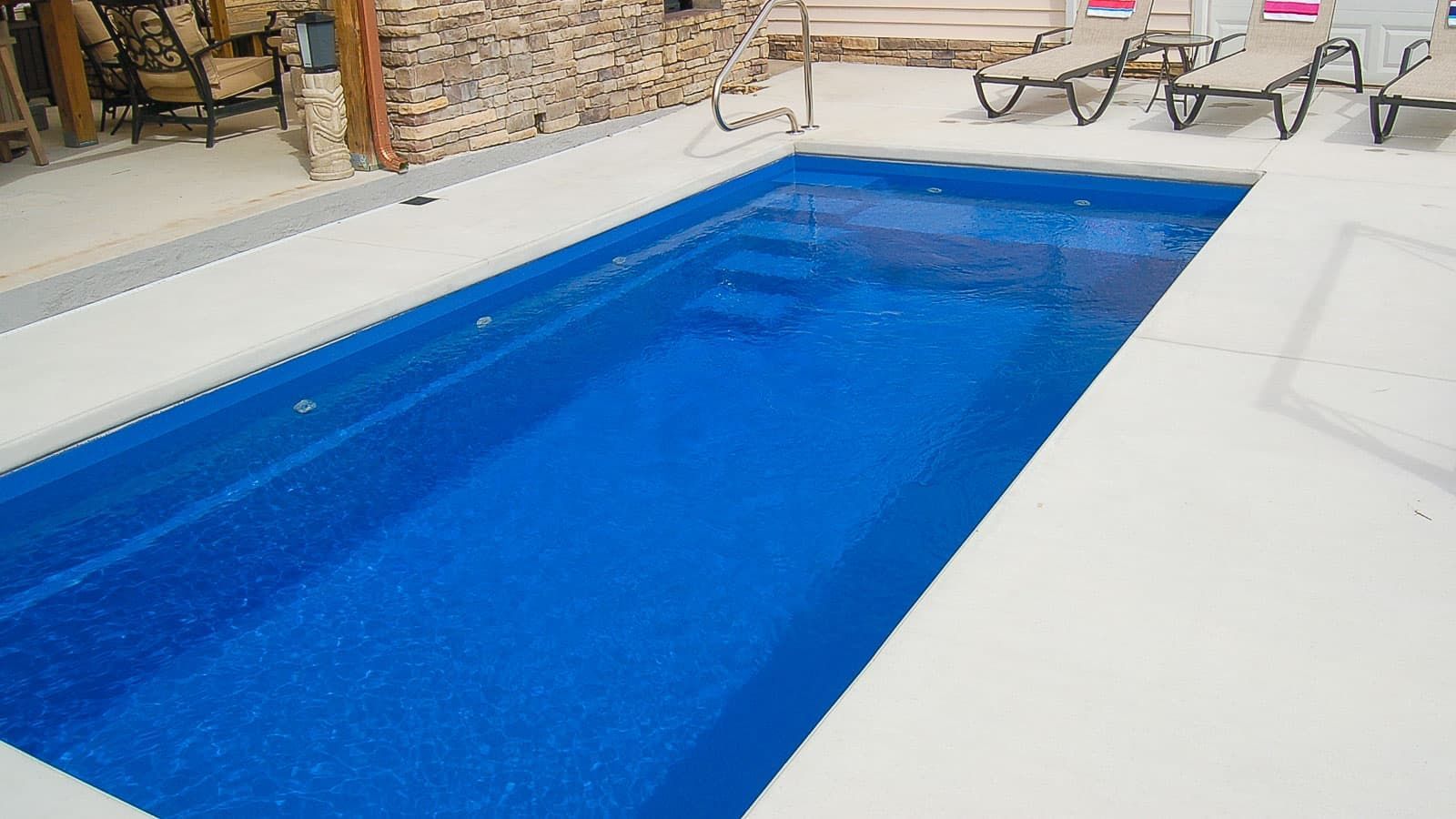 Blue swimming pool beside a white patio with lounge chairs and stone wall in the background