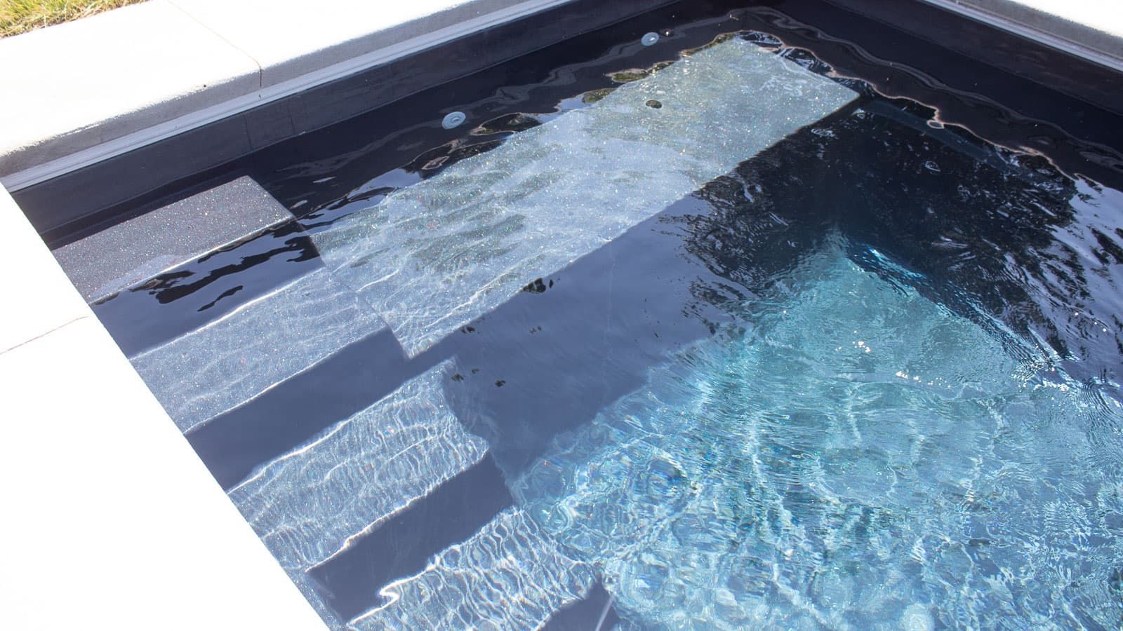 Sunlit blue swimming pool with dark coping and light reflections on the water