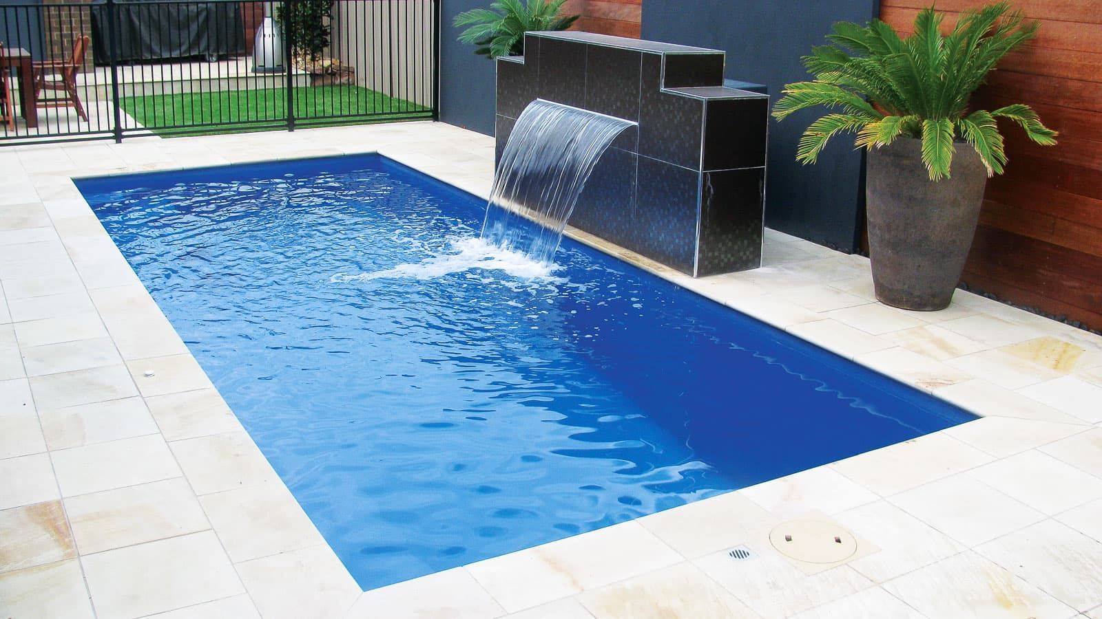 Small blue rectangular pool with a black water feature and potted plant on a tiled patio