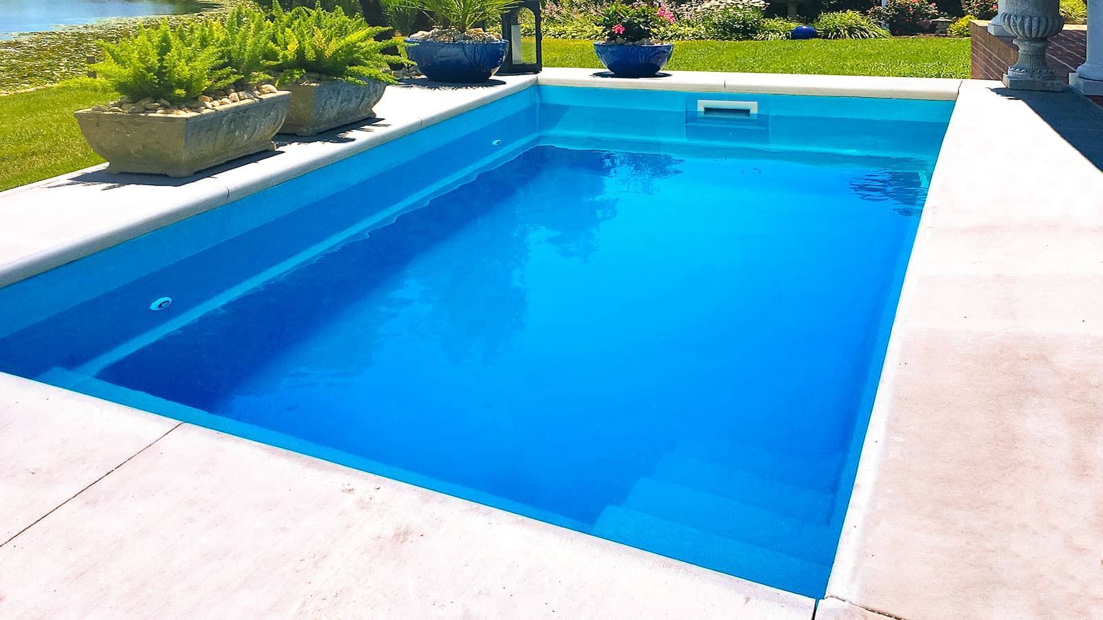 Bright blue swimming pool with white deck and potted plants in a sunny backyard