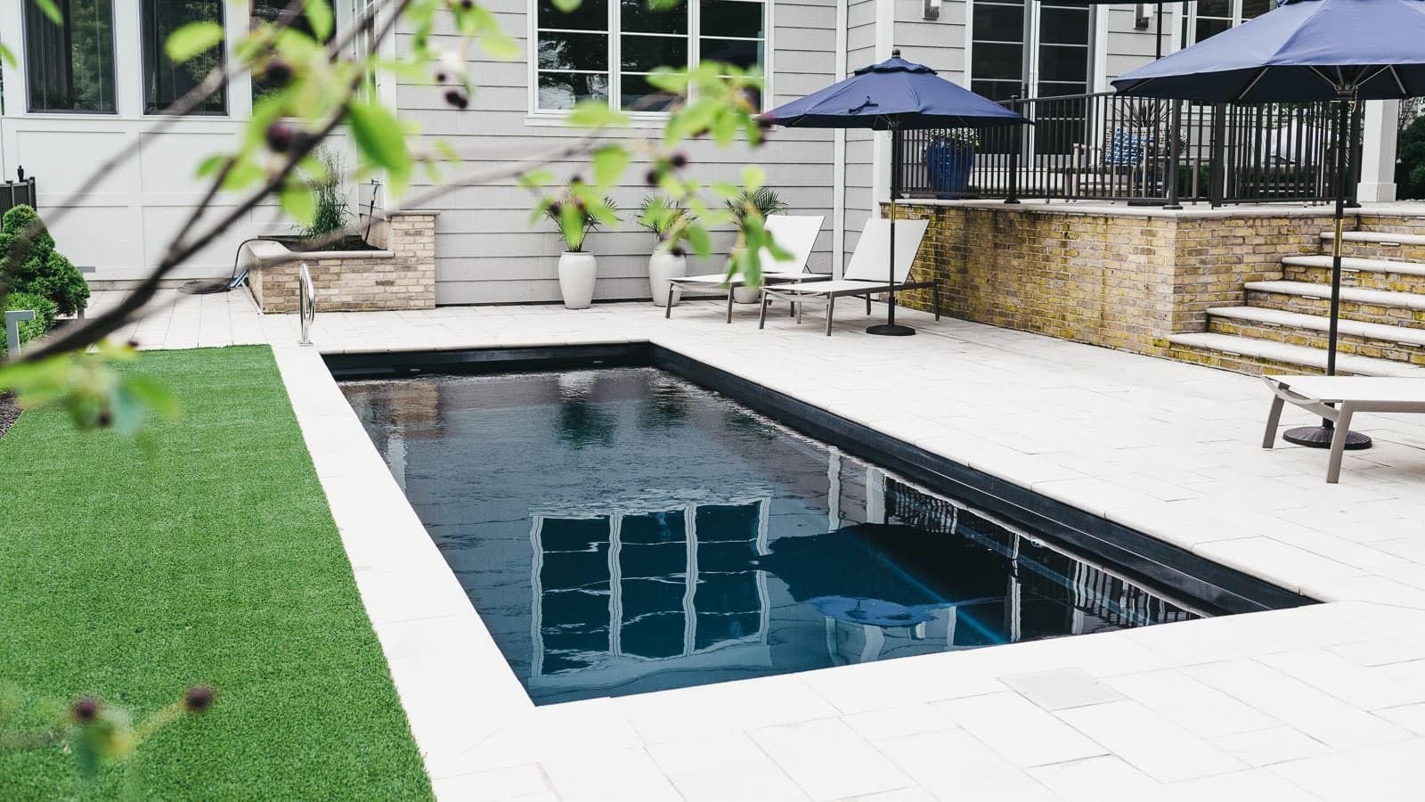 Backyard pool with dark water, white stone deck, grass, lounge chairs, and a patio umbrella