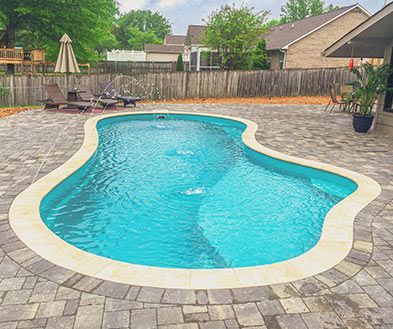 Freeform backyard swimming pool with turquoise water, paver patio, lounge chairs, and wooden fence.
