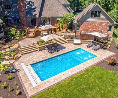 Backyard patio with a rectangular blue pool, lounge chairs, stone steps, and a brick house