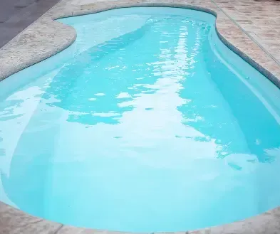 Curved backyard swimming pool with clear turquoise water surrounded by beige stone decking