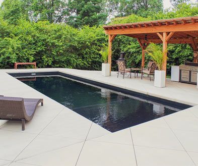 Modern backyard pool with black water, white tile deck, lounge chairs, and a wooden pergola seating area.
