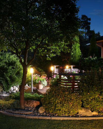 Lit garden path with trees, flowers, and warm lamps beside a home at night