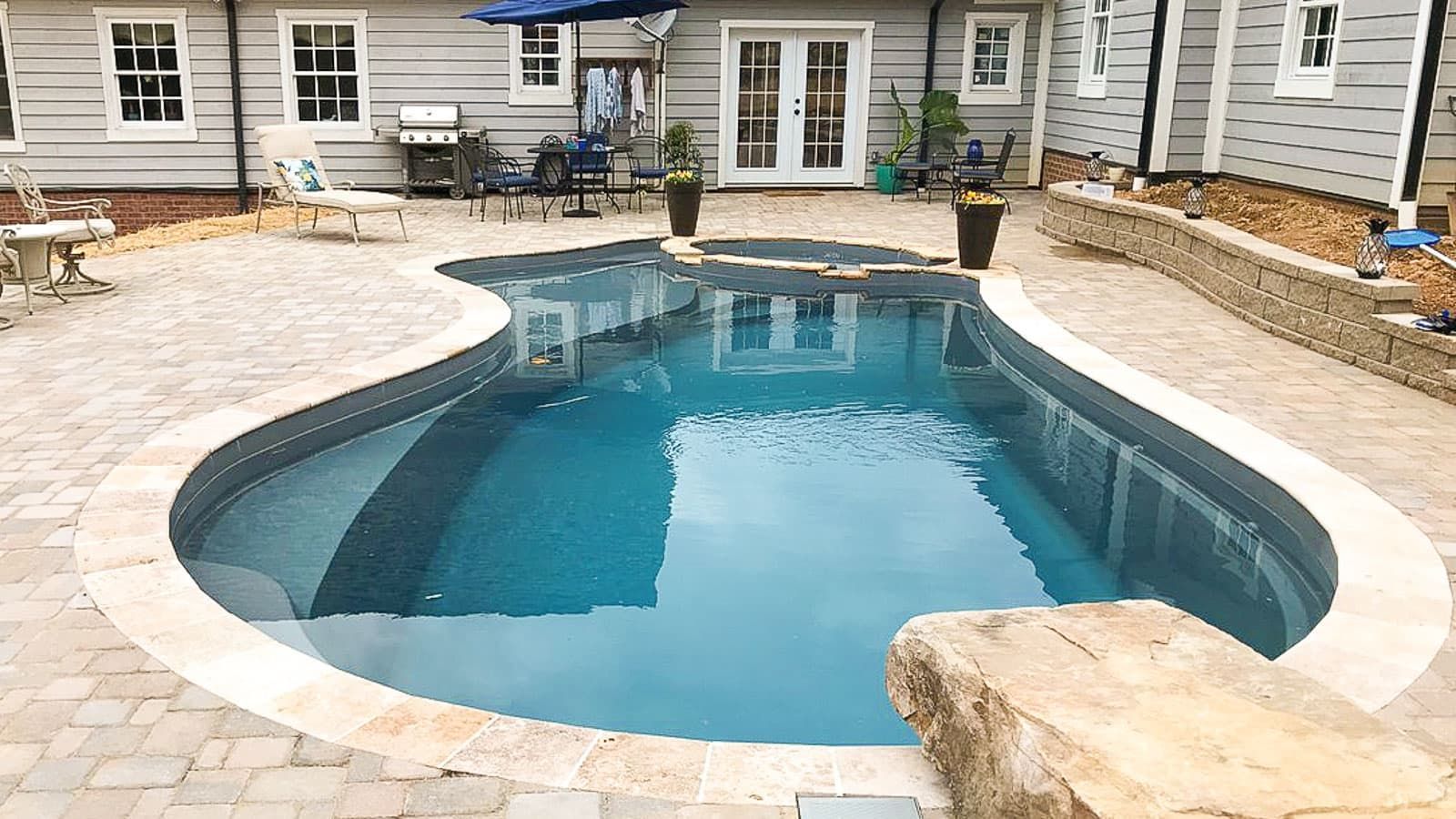 Curved backyard swimming pool with blue water and stone patio beside a house
