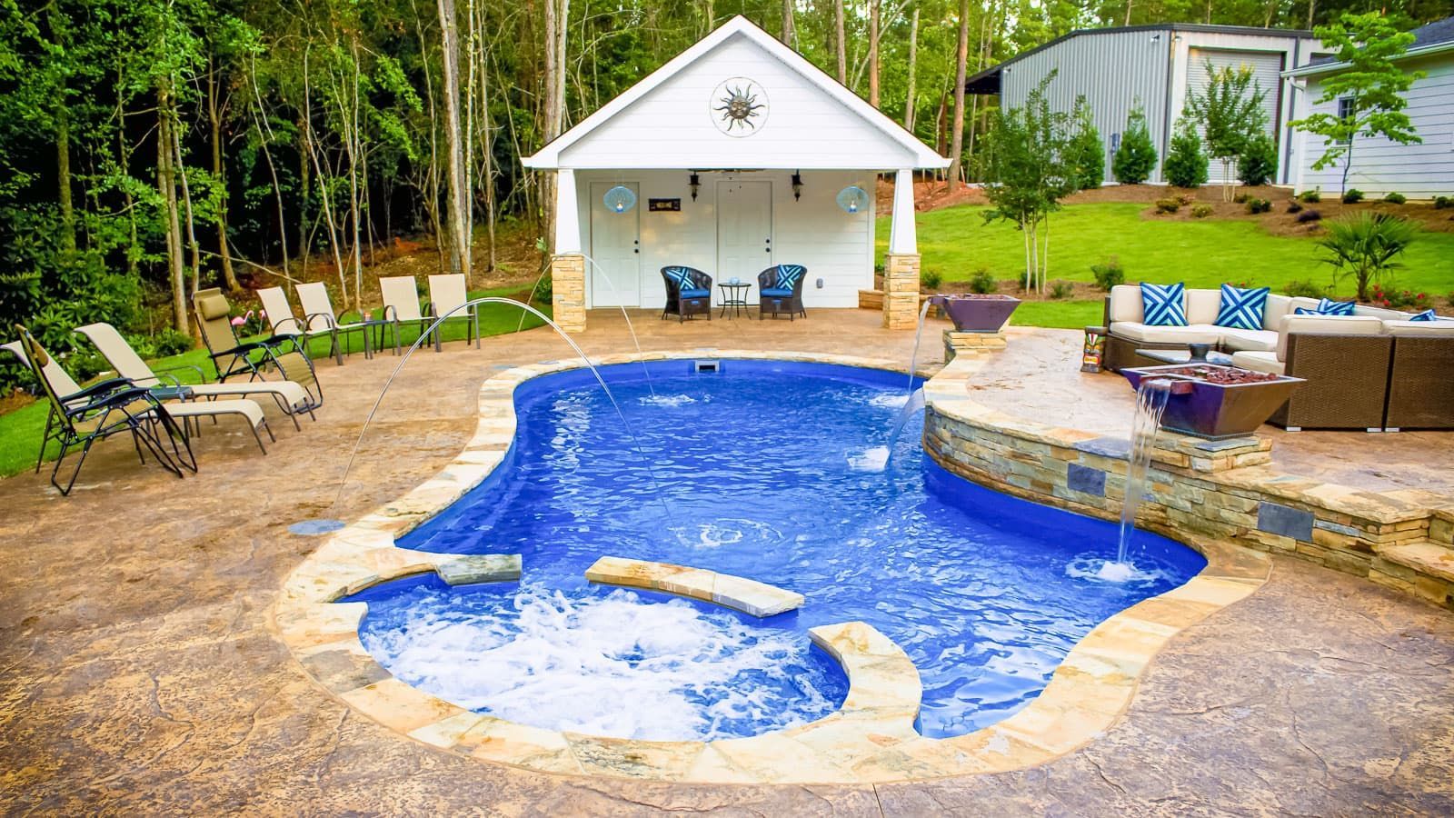 Backyard swimming pool with blue liner, lounge chairs, and a small pool house surrounded by trees
