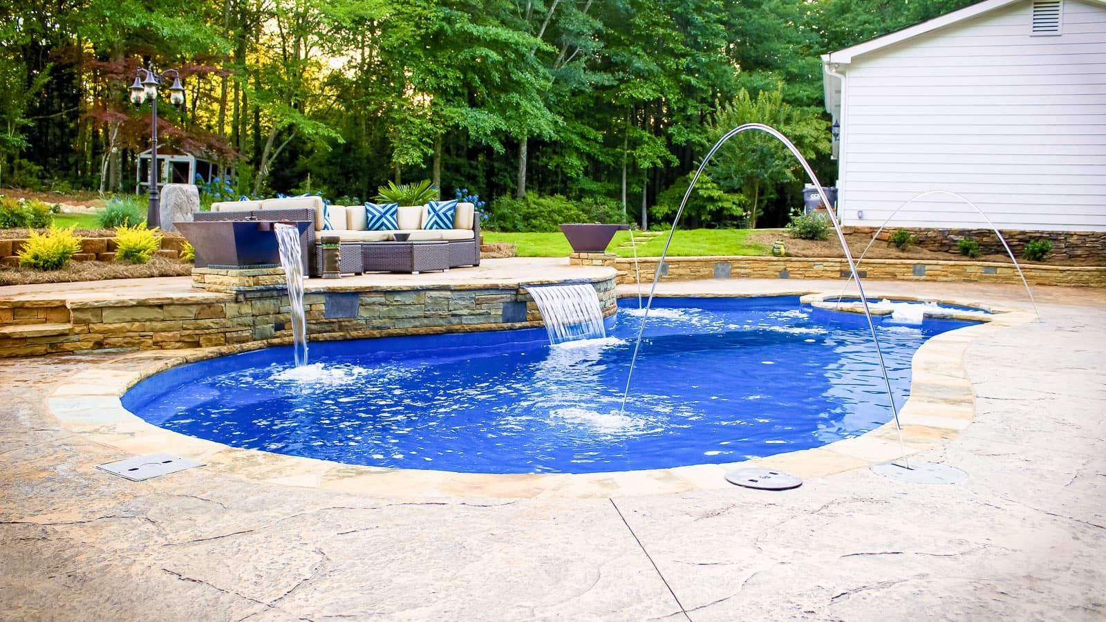 Backyard pool with bright blue water, stone patio, and water fountains spraying into the pool