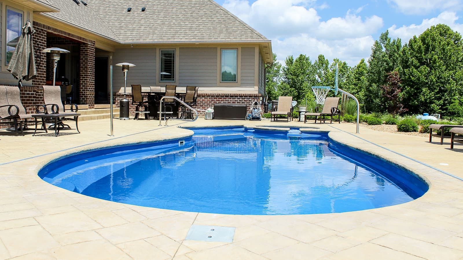 Backyard with a bright blue swimming pool, patio chairs, and a house under a sunny sky