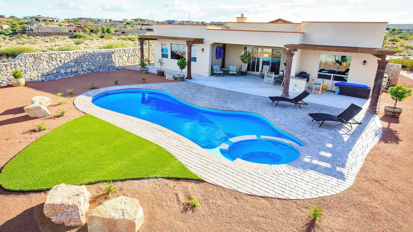 Modern backyard patio with a blue swimming pool, lounge chairs, and desert landscaping