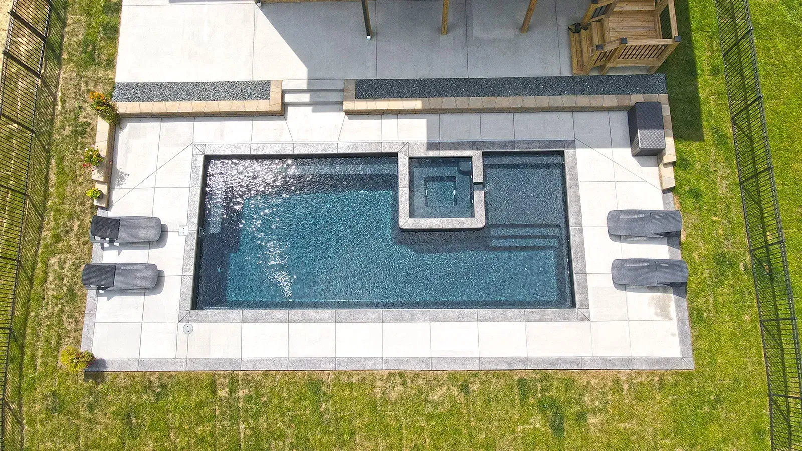 Aerial view of a small rectangular pool with blue water, white stone deck, and surrounding green lawn.