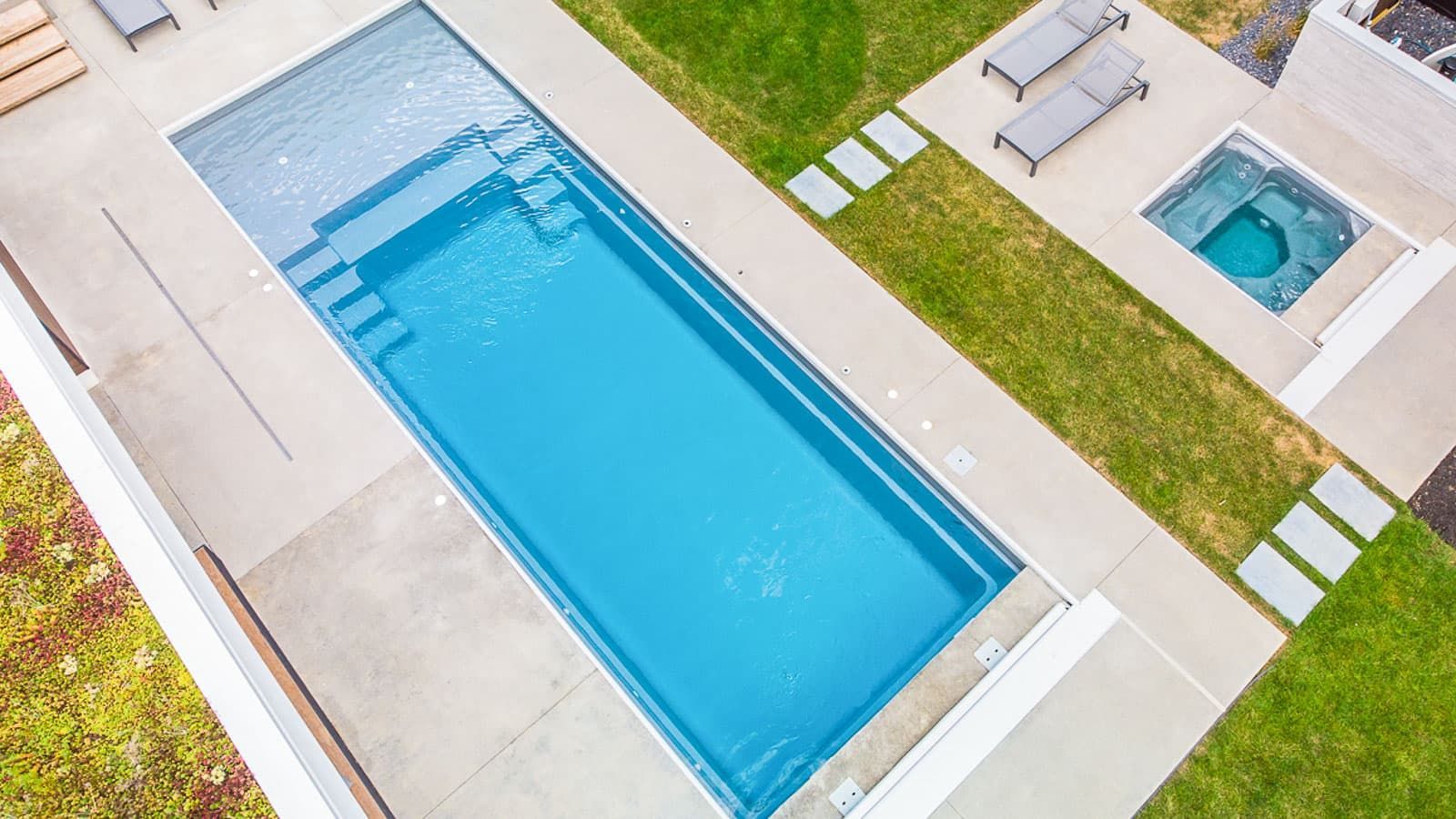 Aerial view of a rectangular outdoor swimming pool with lounge chairs and a hot tub on a landscaped patio.