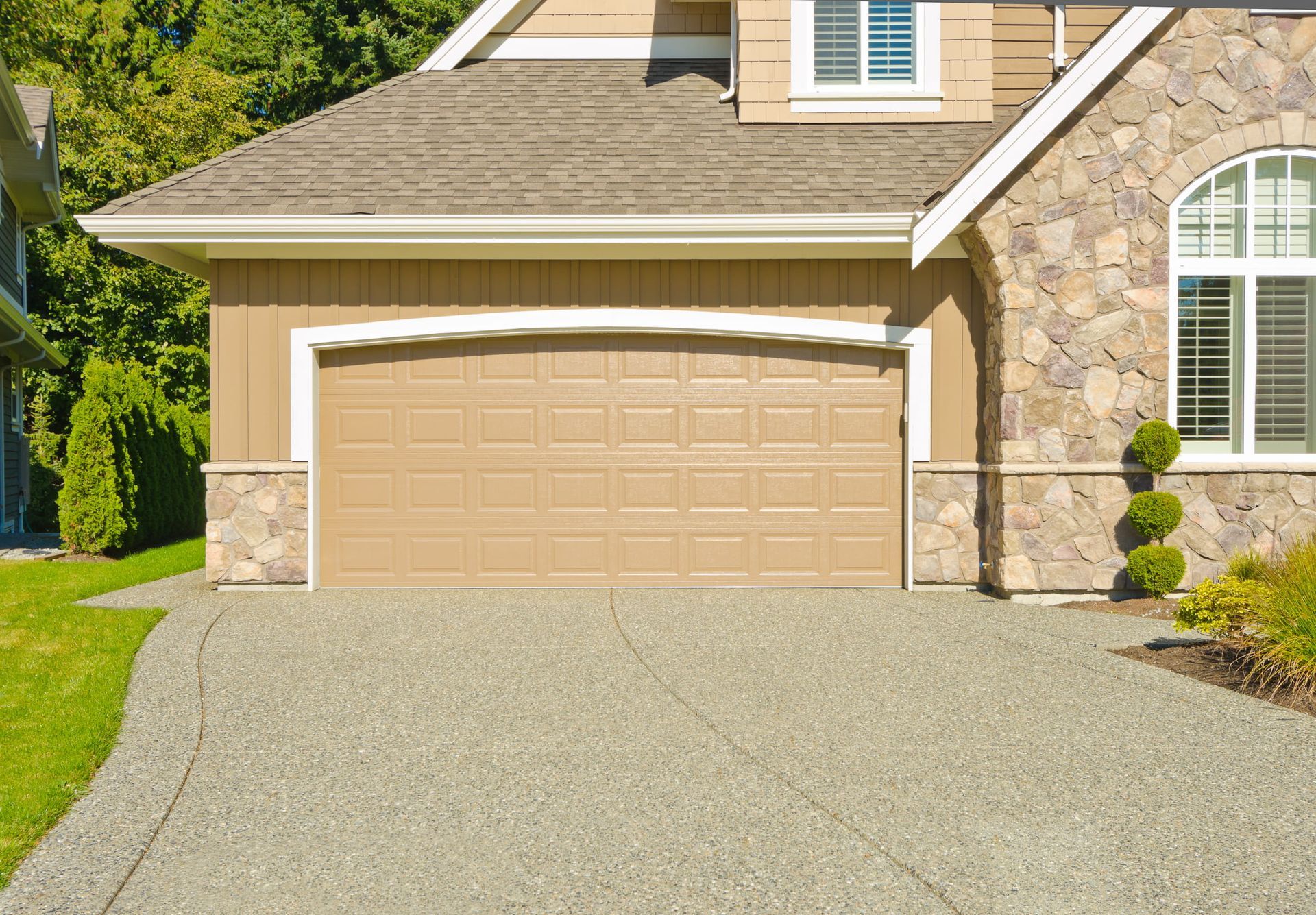 Tan garage door with stone accents, tan siding, and gravel driveway.