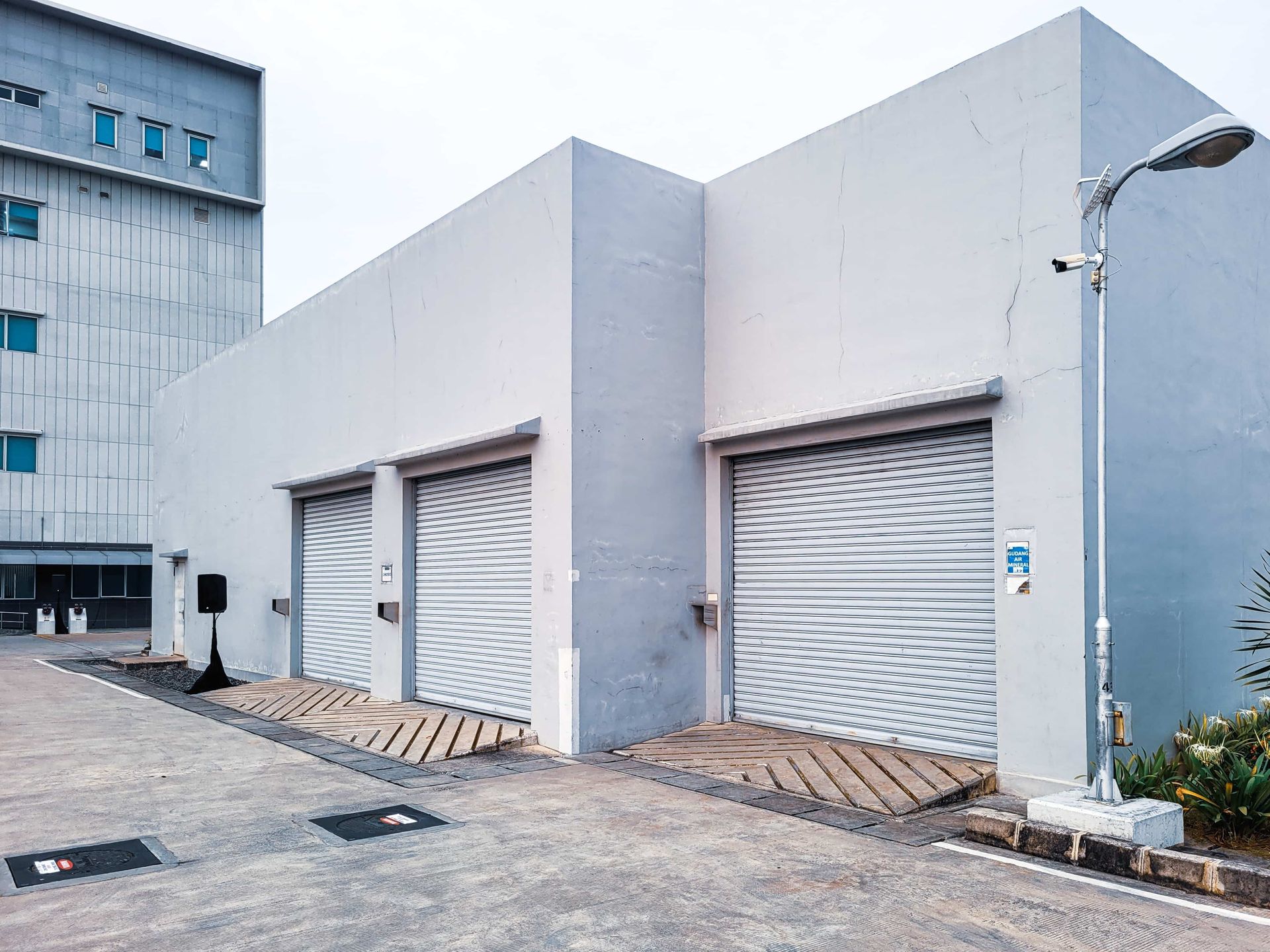 A white industrial building with two loading dock doors and a tall light pole.