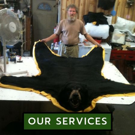 A person stands in a workshop holding a black bear hide with a yellow fabric border behind a 
