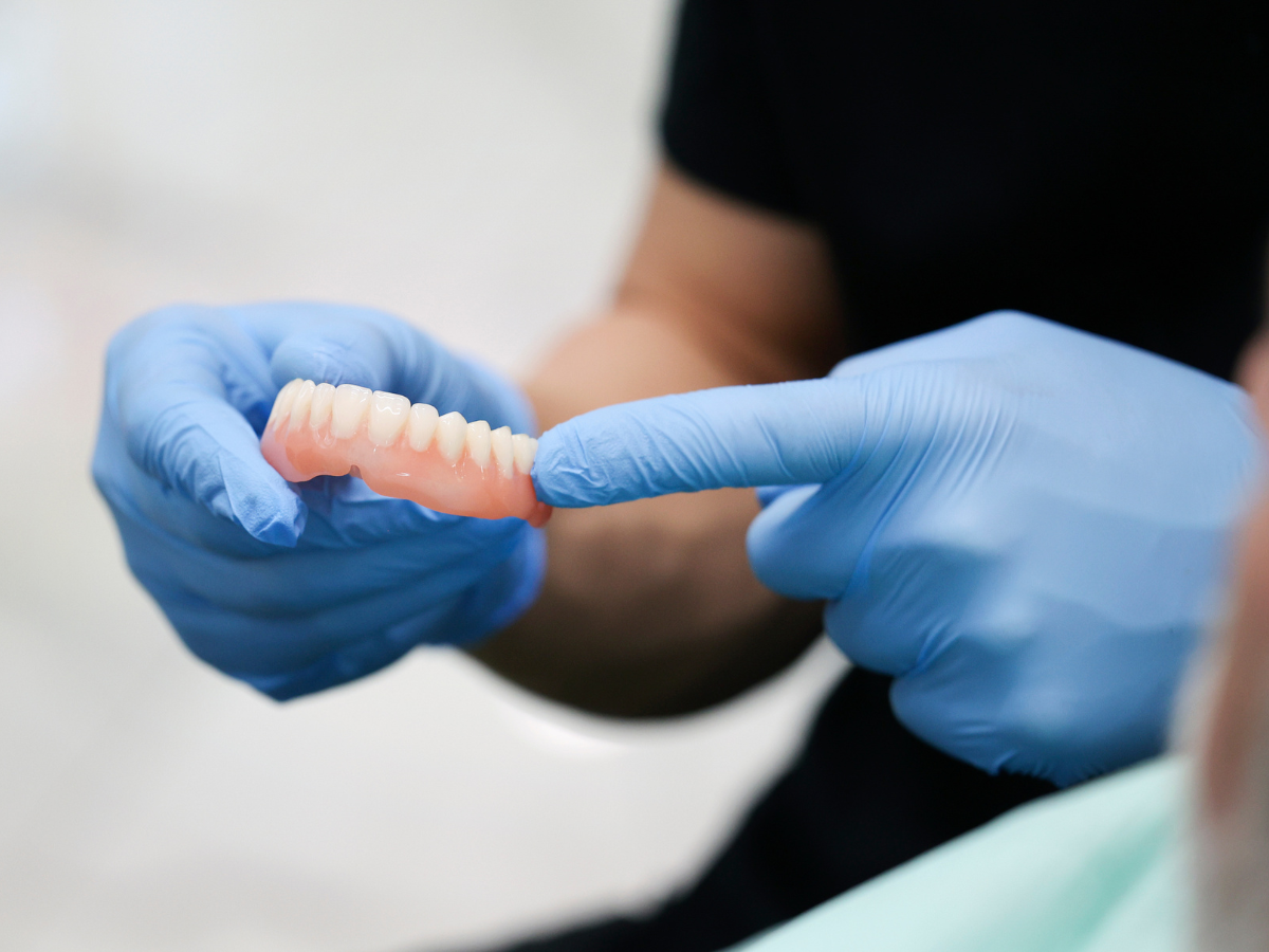 A person wearing blue gloves is holding a denture in their hands.