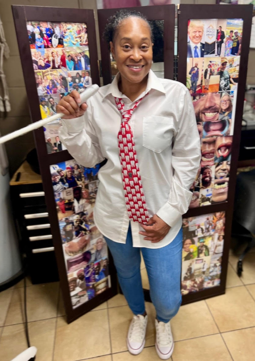 A woman wearing a white shirt and a red tie is standing in front of a collage of pictures.