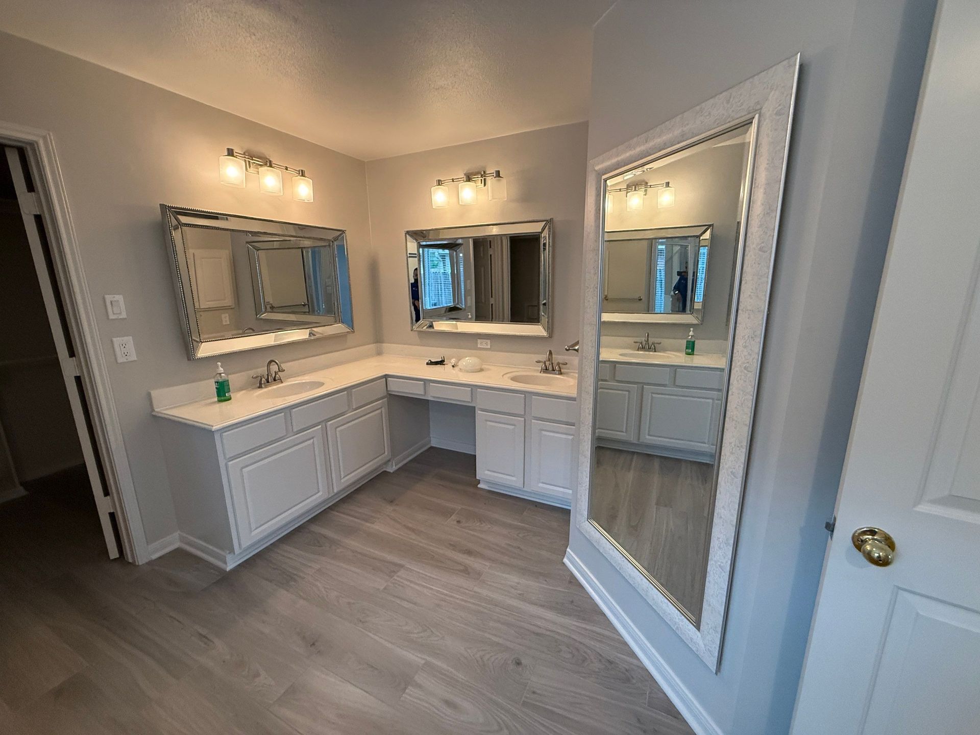 Bathroom with double sinks, large mirrors, and light gray cabinets and walls.