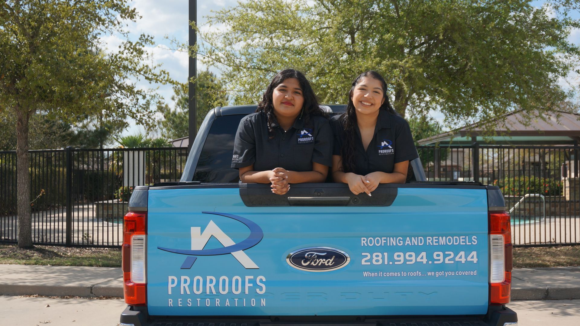 Two people in black shirts in a blue pickup truck bed. 