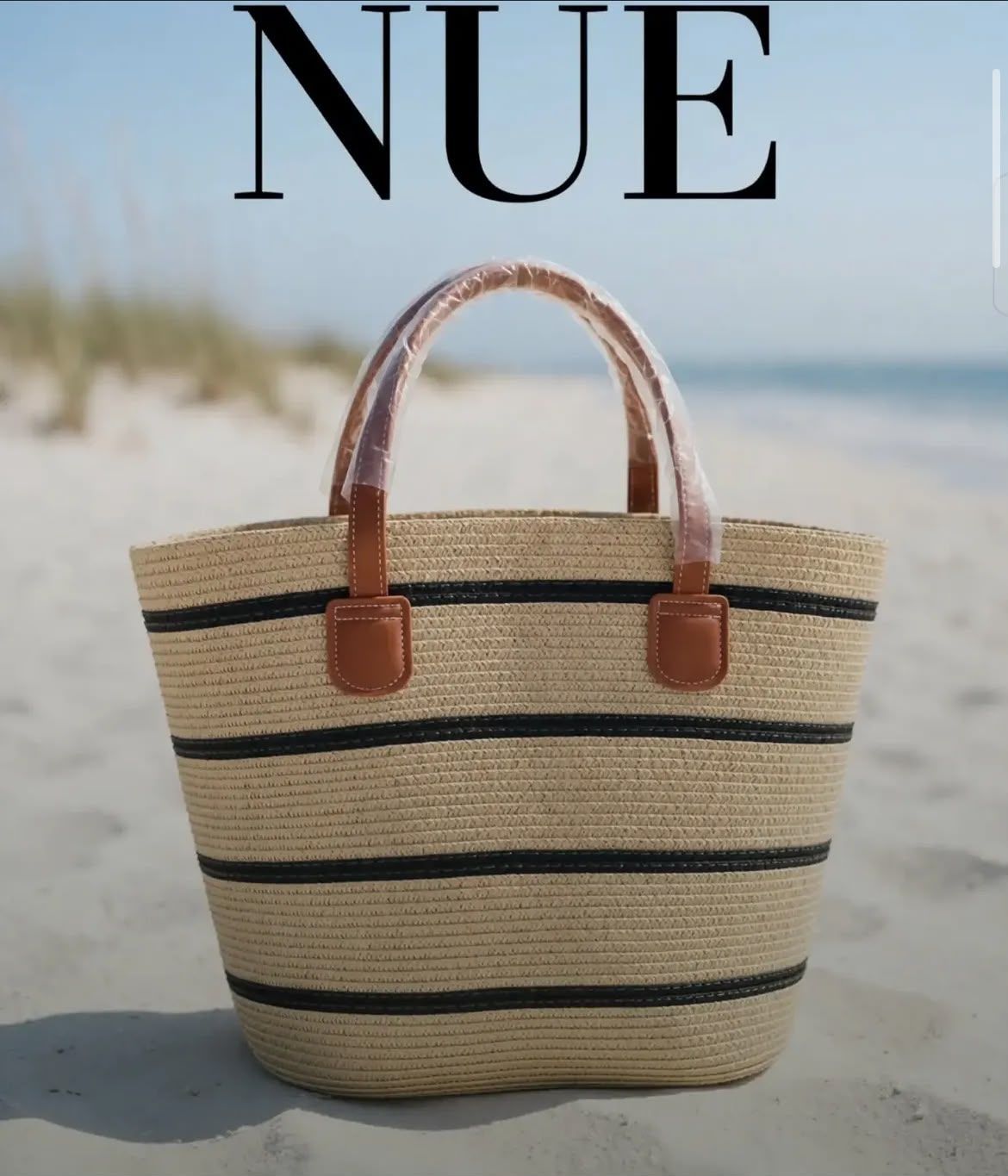 Bolso tote de paja con rayas negras y asas color tostado sobre una playa arenosa, con el texto NUÉ encima