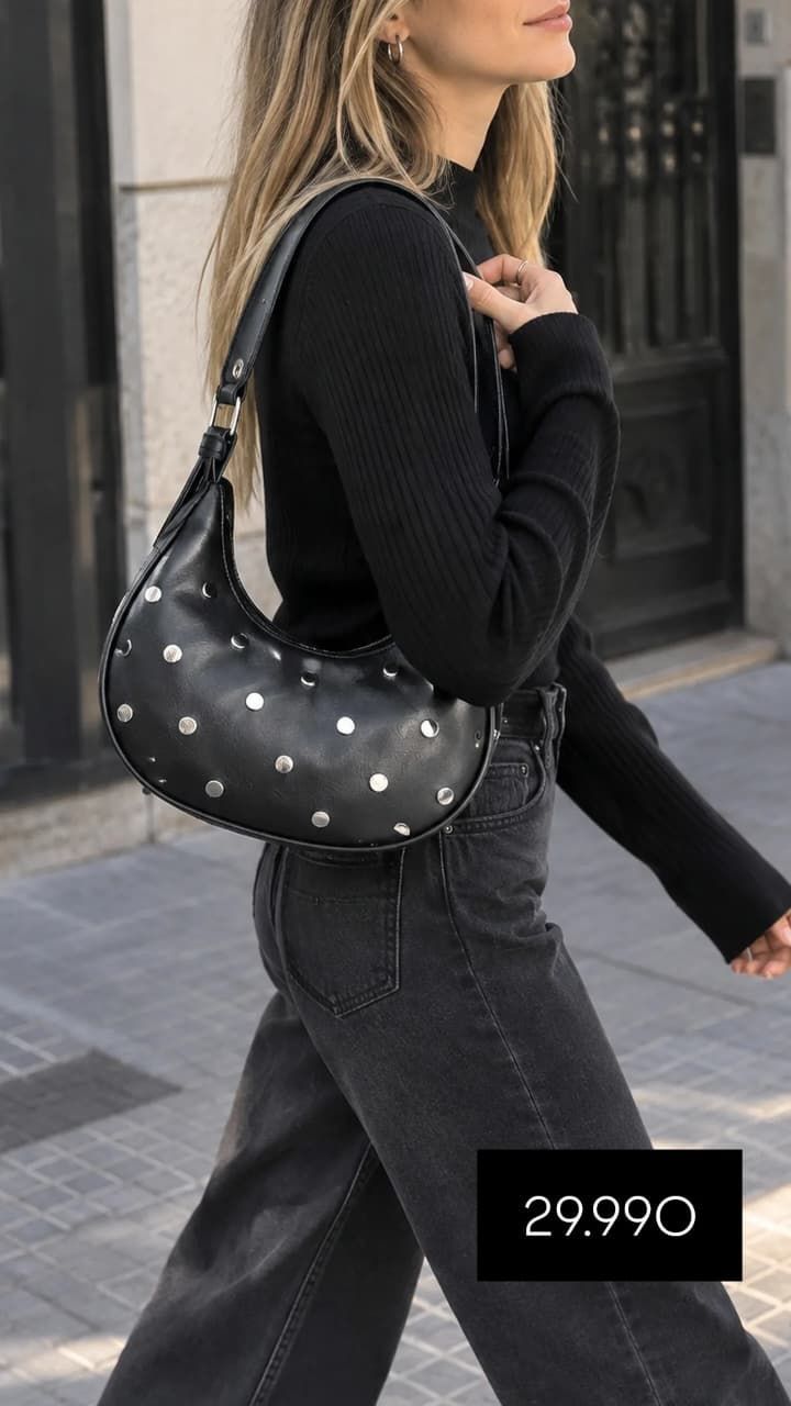 Mujer caminando por una calle de la ciudad con un conjunto negro y un bolso negro con tachuelas.