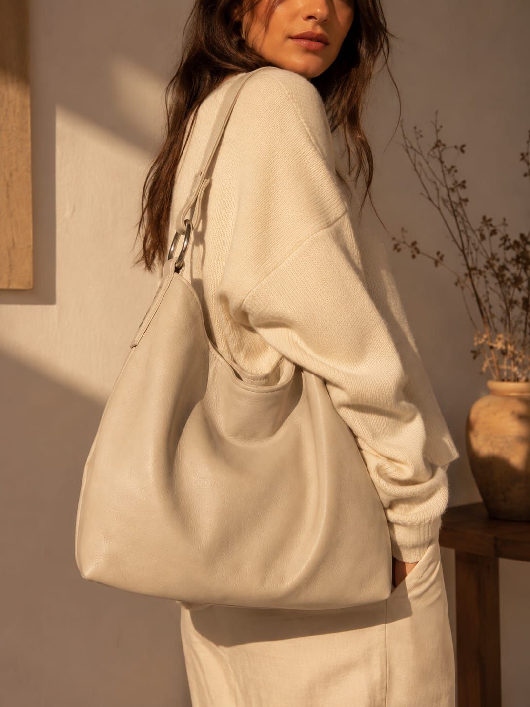 Mujer con un suéter color crema y un bolso grande beige al hombro, bajo una cálida luz interior