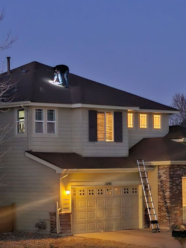 A man is working on the roof of a house at night.