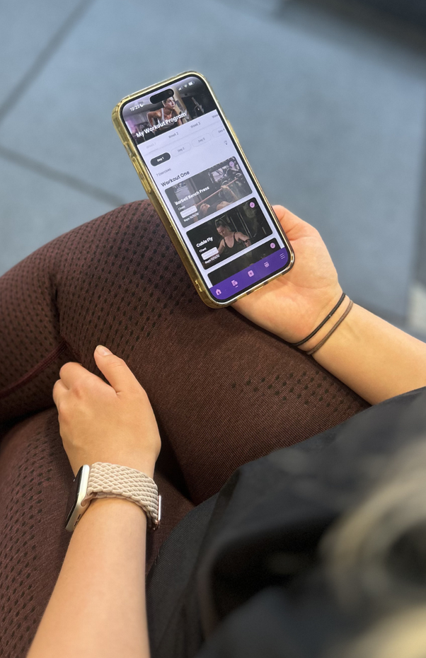 Person holding a smartphone with a purple case while sitting on a brown couch.